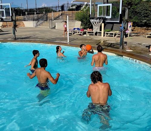 A group of children playing water basketball in a pool on a sunny day.