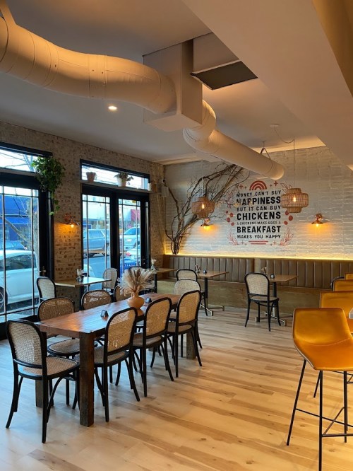 Cozy restaurant interior with wooden tables, chairs, and a wall mural about happiness and breakfast. Warm lighting.
