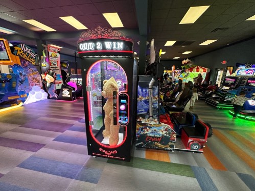 A colorful arcade with various games, featuring a "OUT 2 WIN" prize machine in the foreground.
