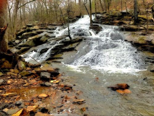 A serene waterfall cascades over rocky terrain, surrounded by trees and a peaceful forest setting.