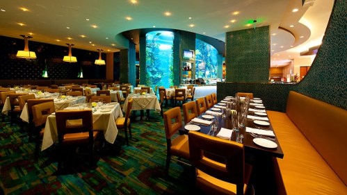 A spacious restaurant with elegant seating, white tablecloths, and a large aquarium in the background.