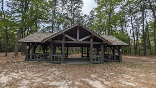 A wooden pavilion surrounded by trees in a park, with a gravel path leading to it.