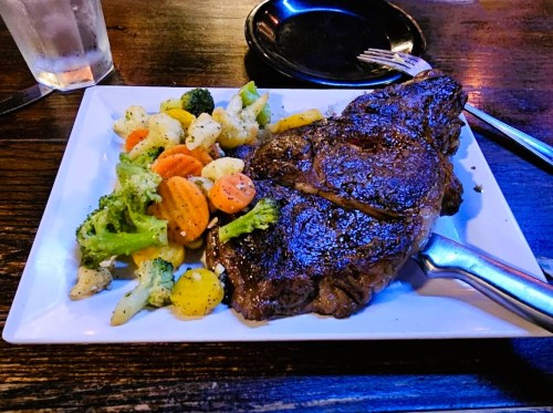 A juicy steak served on a white plate with a side of mixed vegetables, including broccoli, carrots, and cauliflower.