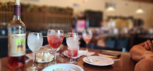 A table with various drinks, including a bottle of rosé, and plates with dessert in a cozy restaurant setting.