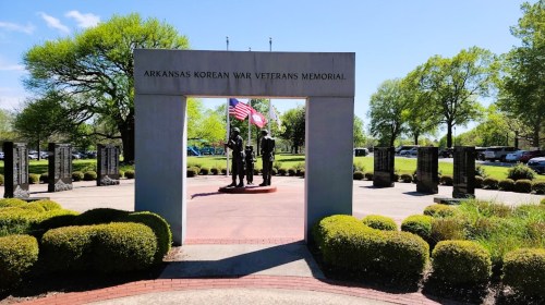 Arkansas Korean War Veterans Memorial featuring statues and flags, surrounded by greenery and pathways.