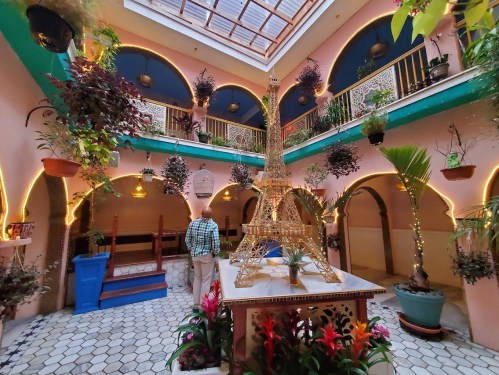 A vibrant indoor courtyard with plants, a model Eiffel Tower, and colorful decor under a skylight.