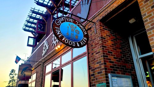 Sign for "Gulfstream Winery" featuring "Fine Food & Ales," with a brick building and sunset in the background.