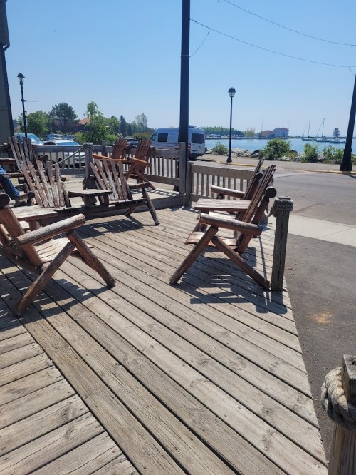 A sunny outdoor deck with wooden chairs overlooking a calm waterfront and distant boats.