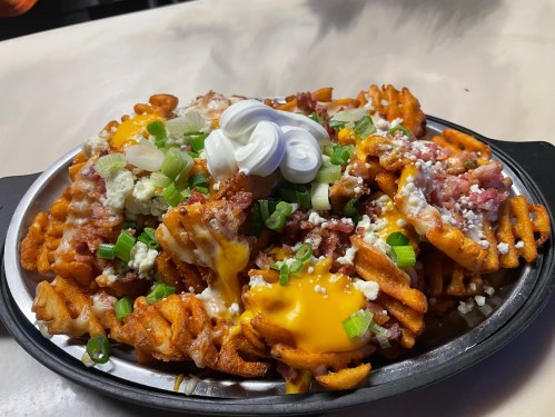 A plate of loaded waffle fries topped with cheese, bacon, green onions, and sour cream.