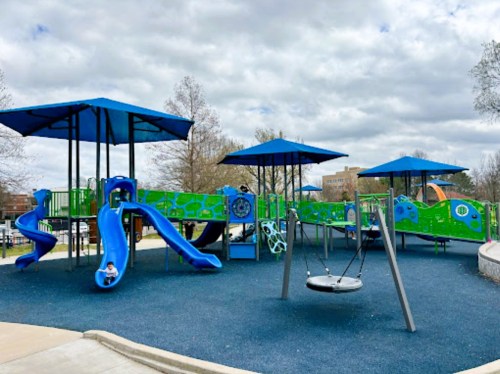 Colorful playground with blue slides, swings, and shaded areas under blue canopies, set against a cloudy sky.