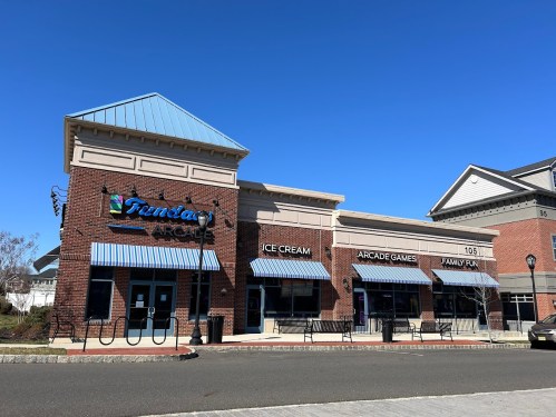 A brick building with blue awnings, featuring signs for ice cream, arcade games, and family fun under a clear blue sky.