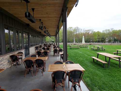 Outdoor dining area with wooden tables and chairs, overlooking a grassy field and trees in the background.