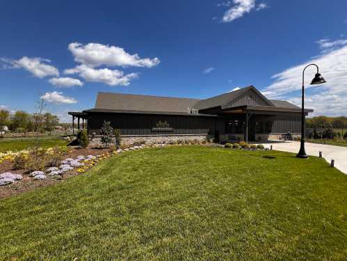 A modern building with a landscaped lawn and colorful flowers under a blue sky with fluffy clouds.