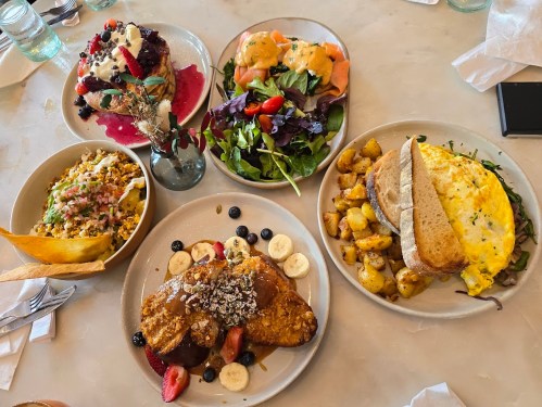 A spread of colorful brunch dishes, including salads, omelets, pancakes, and fruit, arranged on a table.