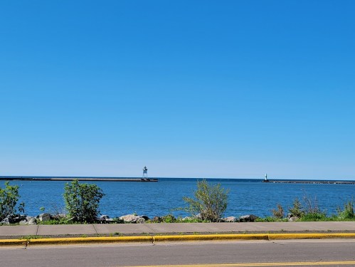 A clear blue sky over a calm lake, with two lighthouses visible in the distance along a rocky shoreline.