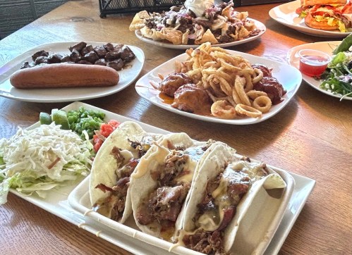 A table spread featuring tacos, nachos, a hot dog, fried onion rings, and a fresh salad.