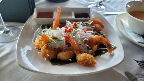 A plate of crispy fried shrimp on a bed of rice noodles, garnished with vegetables and served with dipping sauces.