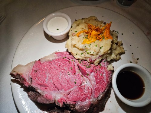 A plate featuring a large slice of prime rib, creamy mashed potatoes, and dipping sauces.