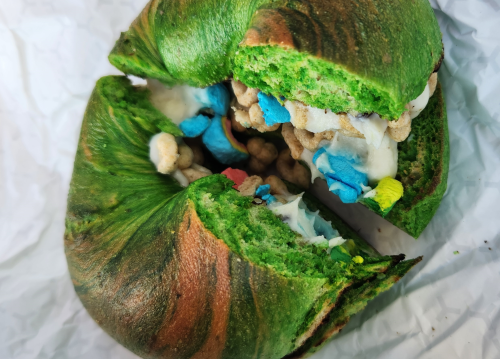 A vibrant green bagel filled with colorful cereal and cream, cut in half to reveal its unique interior.