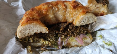 A close-up of a sandwich with a golden-brown crust, filled with green spread, onions, and a savory filling.
