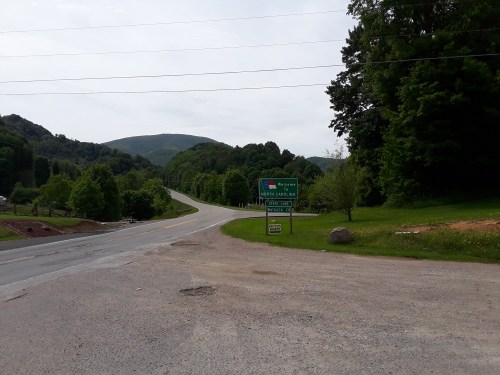 A road sign welcoming visitors to North Carolina, surrounded by green hills and trees on a cloudy day.