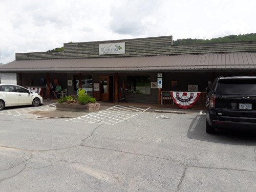 A rustic storefront with a sign reading "Rivercross," featuring patriotic decorations and parked cars in front.