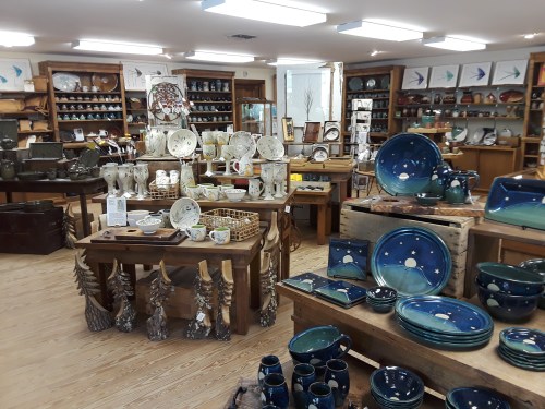 A pottery shop filled with various ceramic dishes, bowls, and decorative items displayed on wooden tables and shelves.