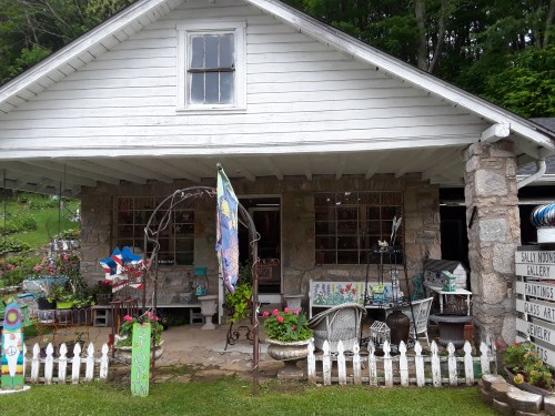 A charming house with a stone facade, colorful decorations, and a garden, featuring a white picket fence and art displays.