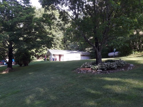 A small house surrounded by trees and a grassy lawn, with a stone garden in the foreground.