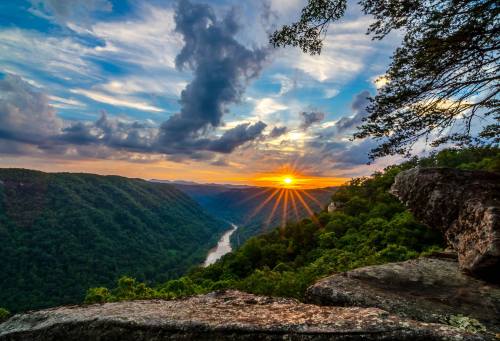 A stunning sunset over a lush valley, with a river winding through and clouds scattered in the sky.
