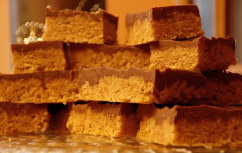 A stack of layered peanut butter bars topped with chocolate, arranged neatly on a glass plate.