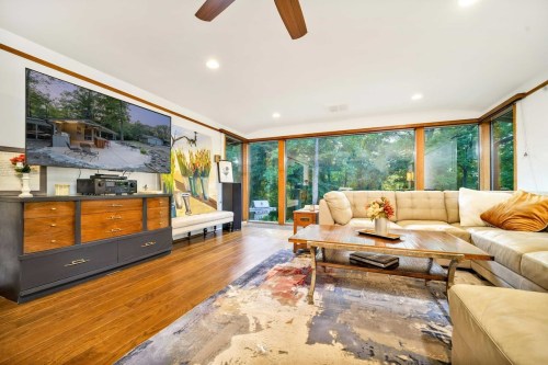 A modern living room with large windows, a sectional sofa, a coffee table, and a TV mounted on the wall.