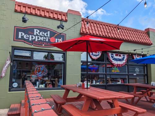 Exterior of The Red Pepperoni Pizzeria with outdoor seating, colorful umbrellas, and festive decorations.