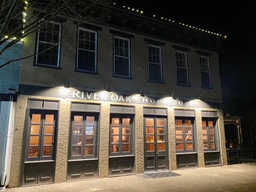 Exterior of River Oak Chop House at night, featuring large windows and illuminated signage.