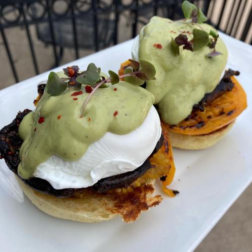 Two poached eggs on toasted English muffins, topped with avocado sauce and garnished with microgreens and red pepper flakes.