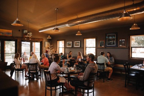A cozy restaurant interior with diners at tables, warm lighting, and artwork on the walls.