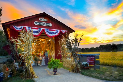 A red barn with festive decorations at sunset, surrounded by fields and autumn plants.