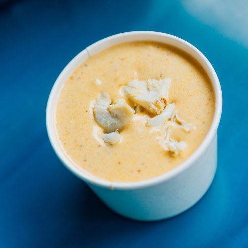 A cup of creamy soup with chunks of seafood, placed on a blue surface.