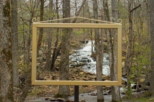 A golden frame stands among trees, showcasing a serene waterfall in the background.