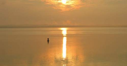 A serene sunset over calm waters, with a golden reflection and a solitary post in the foreground.