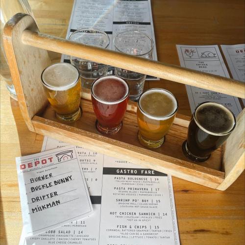 A wooden flight holder with four small beer glasses, alongside menus for food and drinks at a restaurant.