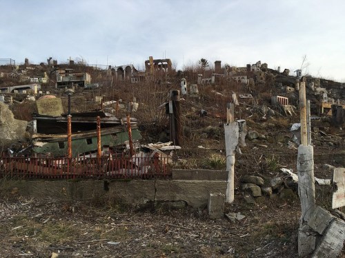 A desolate landscape with abandoned structures and debris scattered across a hillside, under a cloudy sky.
