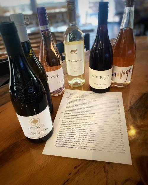 A selection of six wine bottles displayed next to a menu on a wooden table.