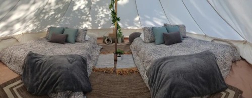 Cozy tent interior with two beds, decorative pillows, a small plant, and a rug, surrounded by soft lighting.