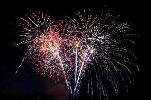 Colorful fireworks burst in the night sky, creating a vibrant display of light and color against a dark background.