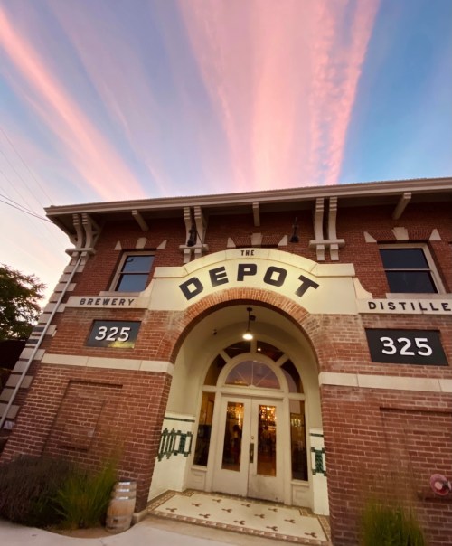The Depot building with a brick facade, large arched entrance, and colorful sunset sky above.