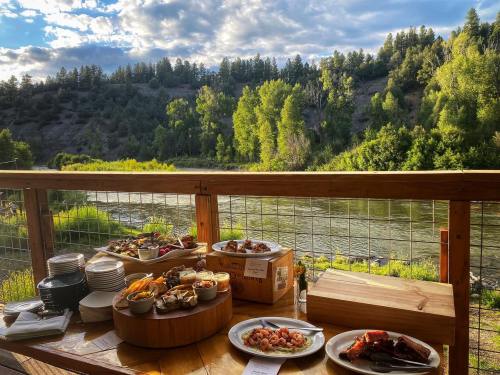 A scenic outdoor dining setup with a variety of dishes, overlooking a river and lush greenery under a cloudy sky.