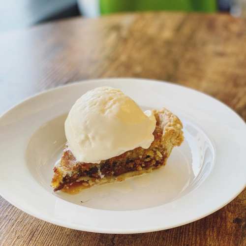A slice of pie topped with a scoop of vanilla ice cream on a white plate, resting on a wooden table.