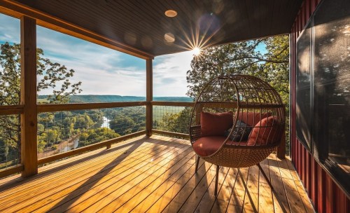 A cozy hanging chair on a wooden deck overlooking a scenic river valley at sunset.