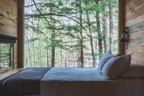 Cozy bedroom with a bed and large window overlooking a serene forest of trees.
